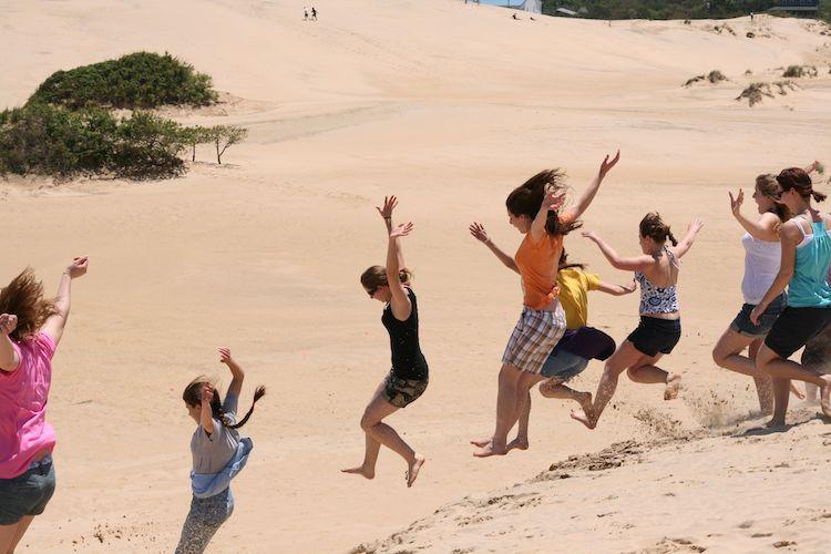 a bunch of kids jumping down a sand dune in nags head nc